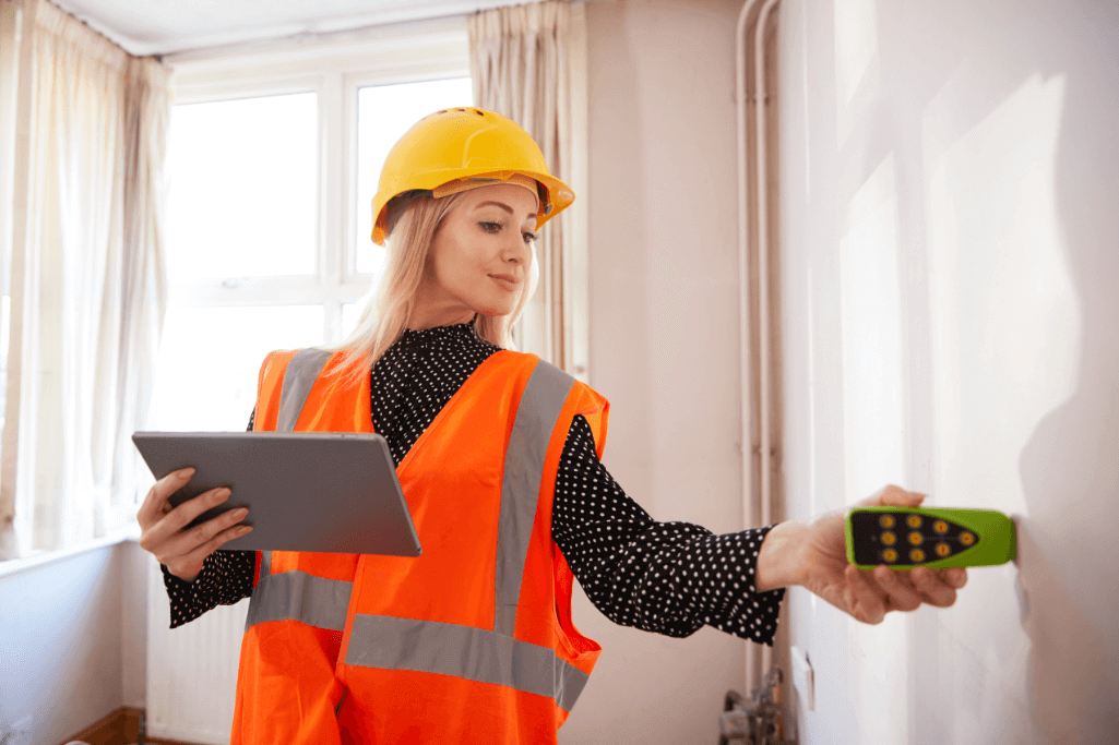 Women in high vis and hard hat is measuring a wall and holding an ipad.