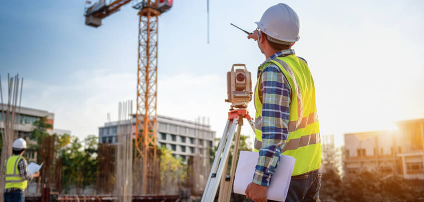 Image of a surveyor surveying a building site.