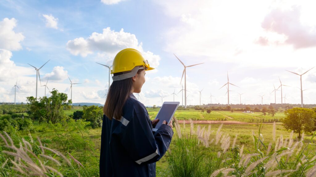 Woman in a hardhat holding an iPad looking at wind turbines. 