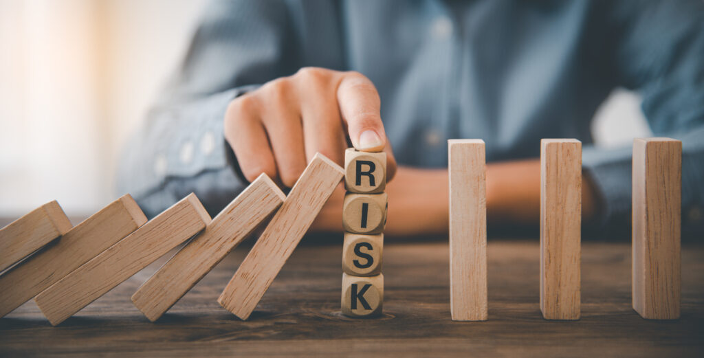 Dominoes being stopped from falling over. The word 'risk' is displayed in between the fallen dominoes and the dominoes still standing. 